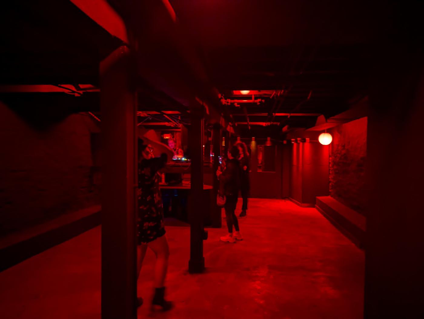 The basement dance floor at tschüss under deep red light, with the DJ booth at the far end