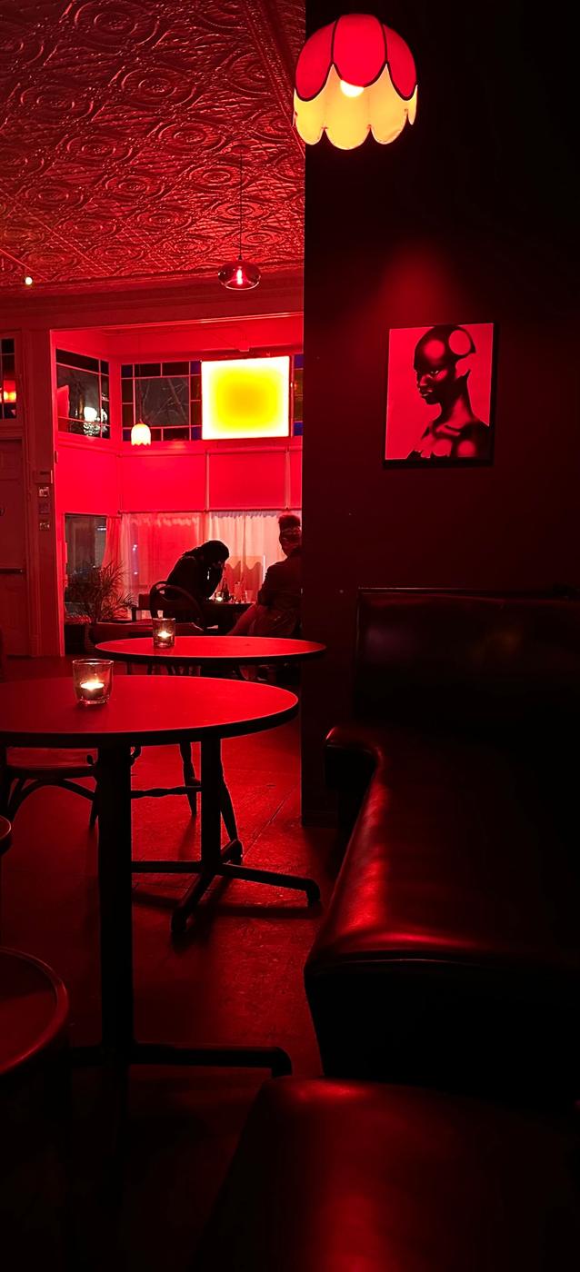 The upstairs bar room at tschüss, lit red, with a pressed tin ceiling, a tulip pendant lamp and candlelit tables